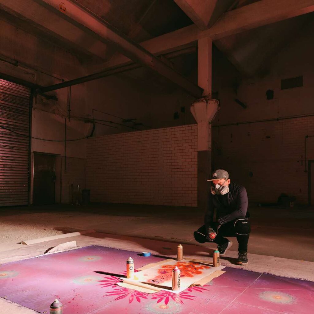 Streetart Künstler Erwa.One bei der Vorbereitung eines riesigen Kunstwerkes mit seinem Designkonzept Neue Ornamente für die Pforzheimer Kulturnacht. Er sitzt in der Hoch vor seinem Kunstwerk welches in Arbeit ist. Er trägt eine Sprühmaske