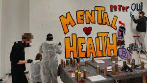Kunstprojekt Mental Health Coach an Schulen. Schüler gestalten mit Sprühdose unter Anleitung des Künstlers Erwa.one ein Wandbild mit dem Schriftzug "mnetale Gesundheit"