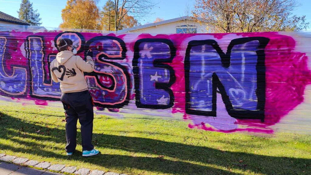 Ein Schüler sprüht Graffiti auf einer mobilen Sprühwand aus Folie