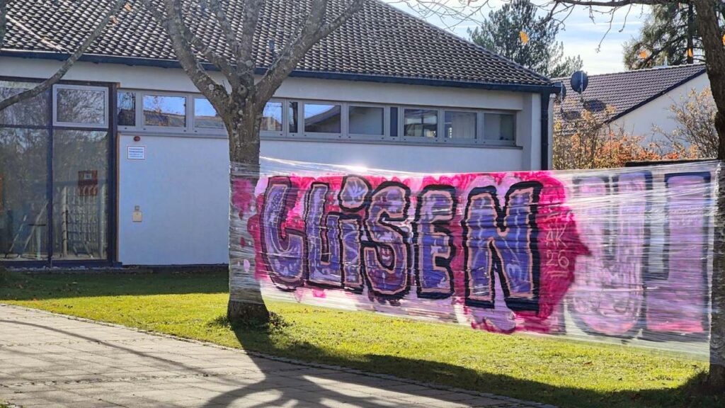 Schule Graffiti Förderzentrum Landsberg mobile Sprühfläche auf Folie aufgespannt zwischen zwei Bäumen. Auf der Sprühfläche ein Graffito mit dem Wort "luisen"
