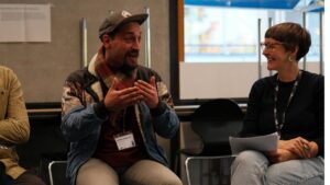 Künstler Erwa.One während seines Redebeitrags zum Thema "Streetart als Change Agent im neuen Klimaregime" im Workshop zum Thema geographische Bildung für planetare Zukünfte. Rechts ist die Wissenschaftlerin Birte Schröder zu sehen
