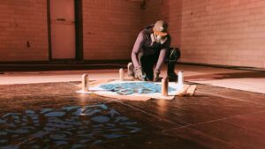 Streetart Künstler Erwa.One bei der Vorbereitung eines riesigen Kunstwerkes mit seinem Designkonzept Neue Ornamente für die Pforzheimer Kulturnacht. Der Künstler kniet in einem ehemaligen Schlachthof auf dem Boden und besprüht eine Plane.