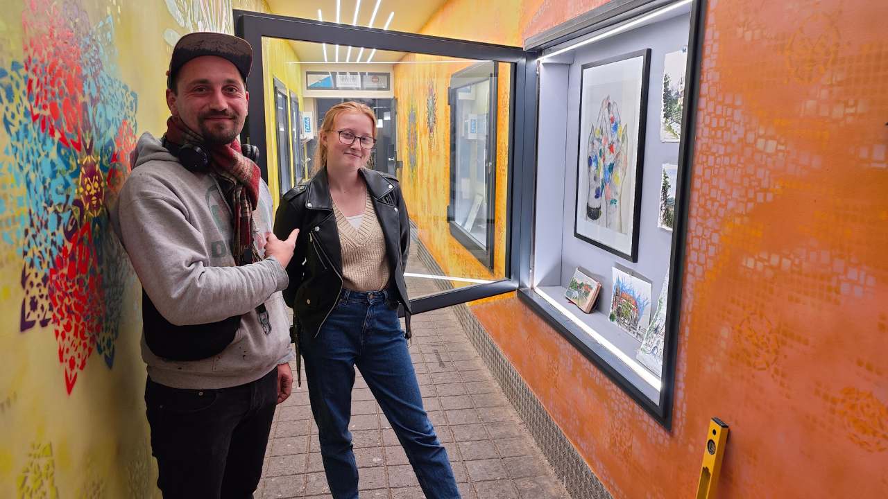 N.E.A. - New emerging artists Ausstellungsreihe in der Zederpassage von Landsberg am lech zeigt neue künstlerische Positionen. Im Bild links: Kurator Vincent Göhlich aka Erwa.One und rechts Kunststudentin Daniela Steidl. Schaufenster ist offen. Darin befindet sich Kunstwerke aus Aquarellen Urban Sketching von Gebäuden und Städten