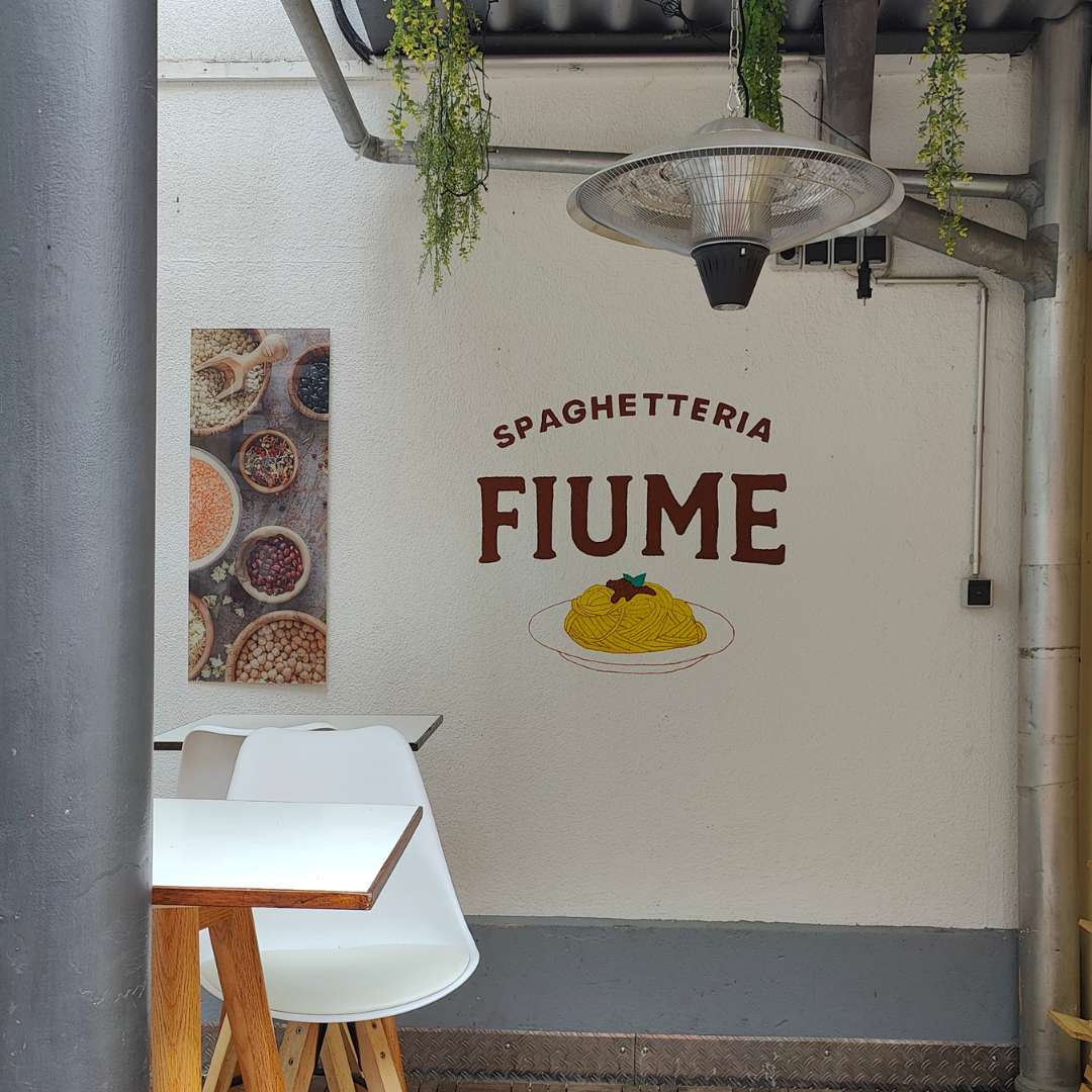 B2B Auftragsgestaltung für einen Gastronomiebetrieb Fiume in Landsberg am Lech. Ausschnitt auf Terrasse Schriftzug Spaghetteria Fiume in Siena-Braun darunter Motiv spaghetti gemalt mit Pinsel