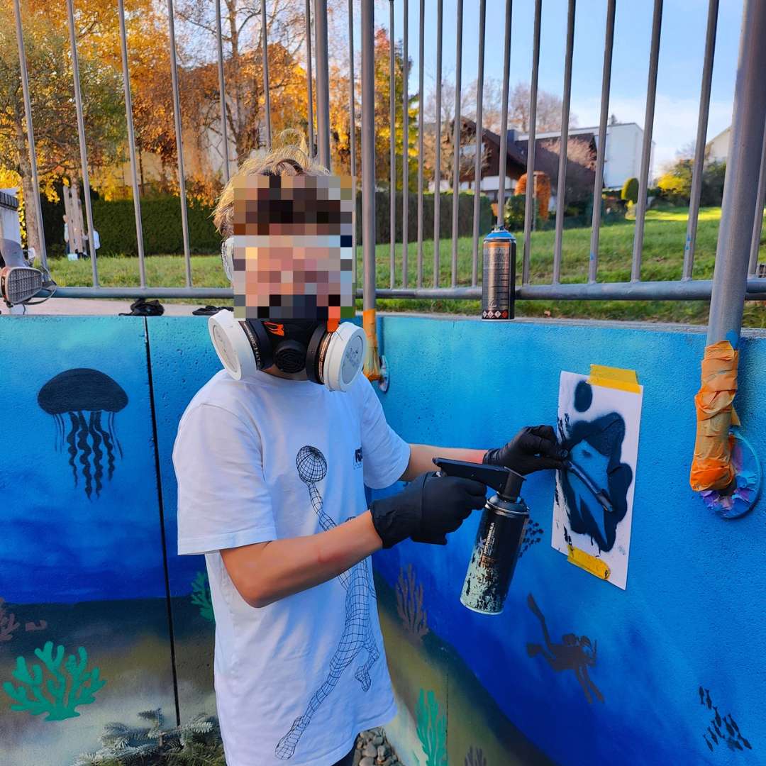 Kunstprojekt offene Jugendarbeit in Pöcking am Starnberger See. Thema des Streetart-Projektes "Unterwasserwelt" auf einer Betonmauer am Schwimmbad von Pöcking. Eine Junge hält einen Stock auf eine Schablone und in der anderenHand eine Sprühdose