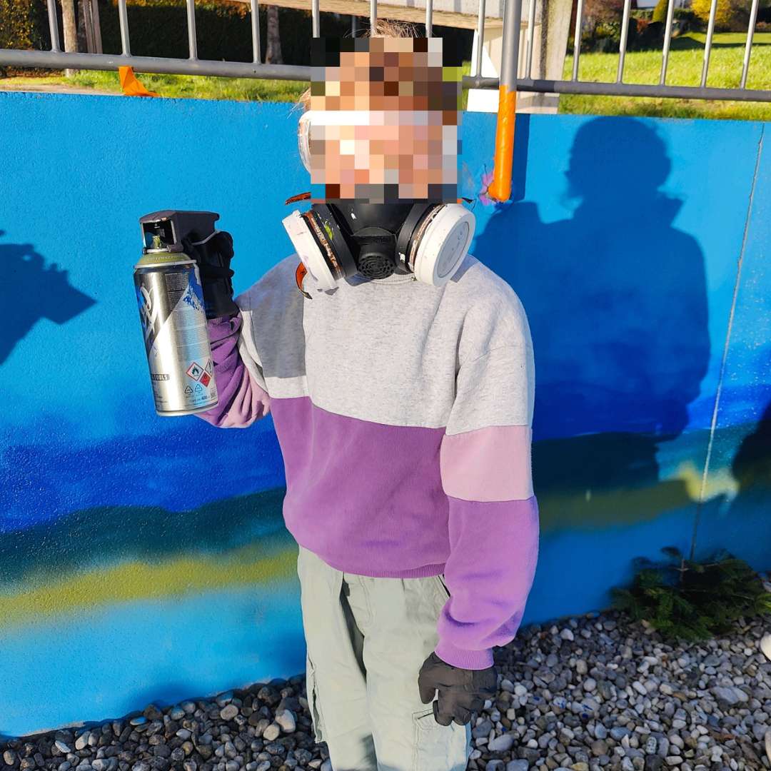 Kunstprojekt offene Jugendarbeit in Pöcking am Starnberger See. Thema des Streetart-Projektes "Unterwasserwelt" auf einer Betonmauer am Schwimmbad von Pöcking. Anonymisierte Teilnehmerin hält eine Sprühdose in die Kamera und trägt eine FFP3-Schutzmaske