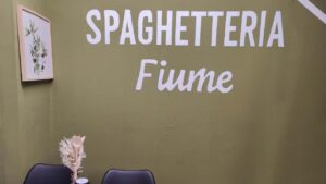 B2B Auftragsgestaltung für einen Gastronomiebetrieb Fiume in Landsberg am Lech. Ausschnitt auf Innenraum der Gastronomie mit Schriftzug "Spaghetteria Fiume" in weiß und einem neo-traditionallem Inneneinrichtungslook.