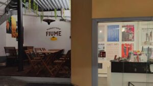 B2B Auftragsgestaltung für einen Gastronomiebetrieb Fiume in Landsberg am Lech. Ausschnitt auf bestuhlte Terrasse mit Auftragsarbeit im Hintergrund auf der Wand. Rechts ist das Büro des Galerievereins Landsberg zu sehen.