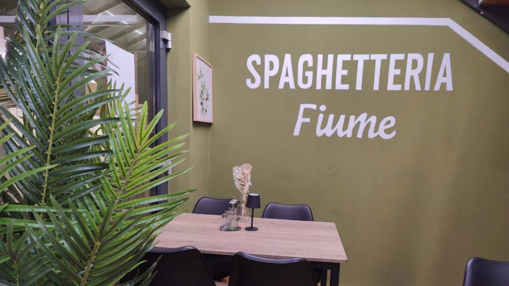 B2B Auftragsgestaltung für einen Gastronomiebetrieb Fiume in Landsberg am Lech. Ausschnitt auf Innenraum der Gastronomie mit Schriftzug "Spaghetteria Fiume" in weiß und einem neo-traditionallem Inneneinrichtungslook.