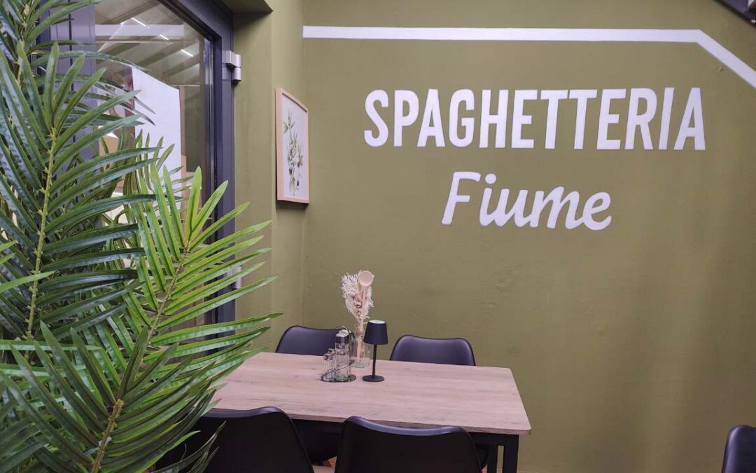 B2B Auftragsgestaltung für einen Gastronomiebetrieb Fiume in Landsberg am Lech. Ausschnitt auf Innenraum der Gastronomie mit Schriftzug "Spaghetteria Fiume" in weiß und einem neo-traditionallem Inneneinrichtungslook.