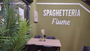 B2B Auftragsgestaltung für einen Gastronomiebetrieb Fiume in Landsberg am Lech. Ausschnitt auf Innenraum der Gastronomie mit Schriftzug "Spaghetteria Fiume" in weiß und einem neo-traditionallem Inneneinrichtungslook.