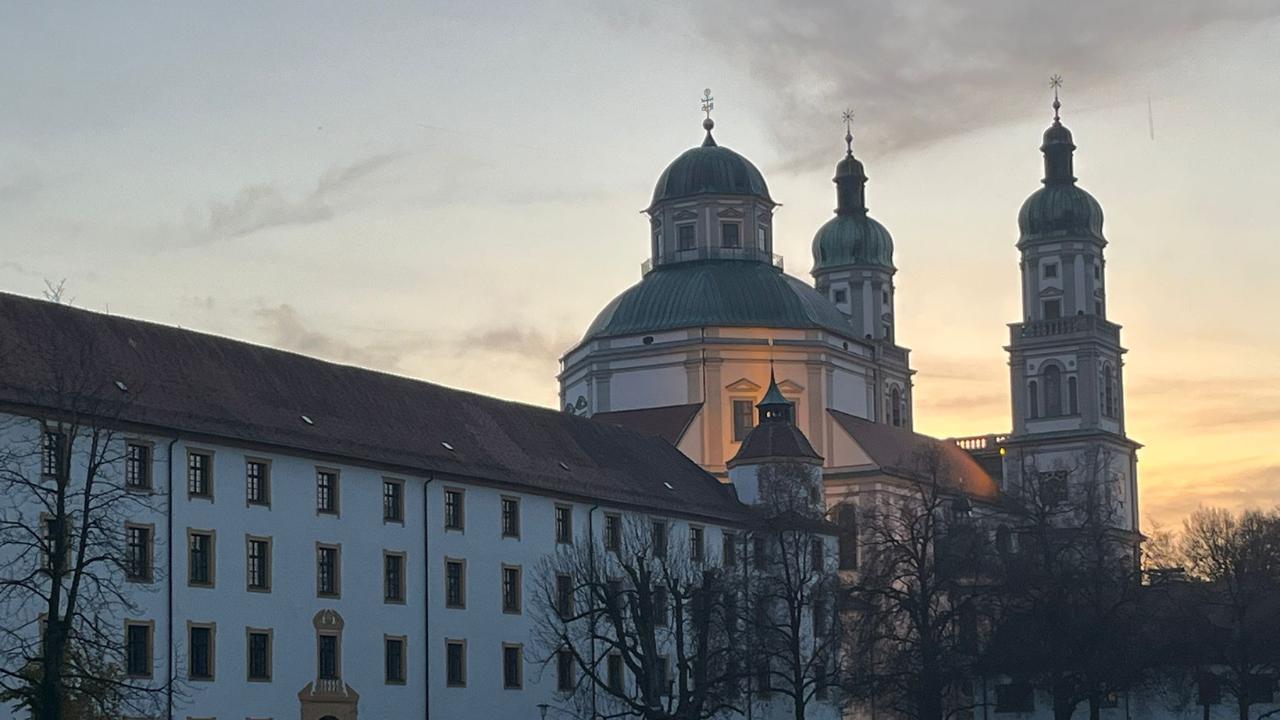 Blick auf die Residenz Kempten und den darin liegenden Hofgartensaal bei herbstlicher Dämmerung. Das Abendlicht lässt die Barock-Architektur in einem orangen Schimmer Glimmern.
