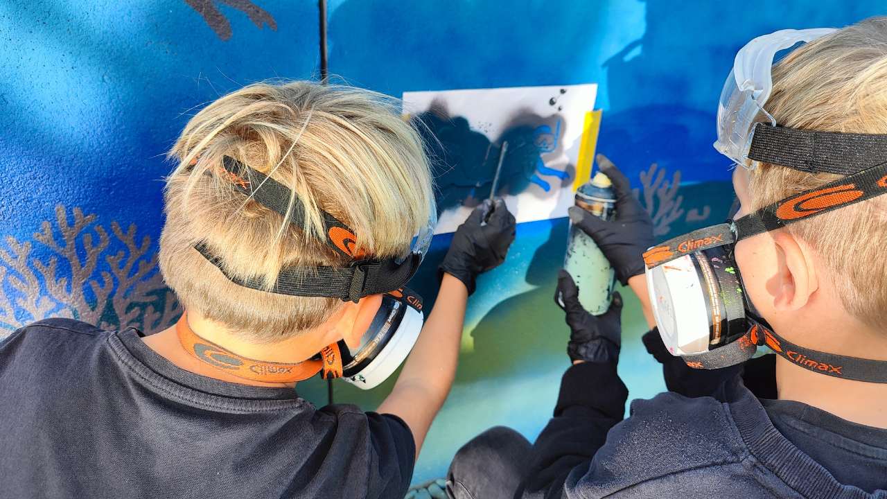 Kunstprojekt offene Jugendarbeit in Pöcking am Starnberger See. Thema des Streetart-Projektes "Unterwasserwelt" auf einer Betonmauer am Schwimmbad von Pöcking. Zwei Jungs sprühen eine Schablone auf eine Wand in Teamarbeit.