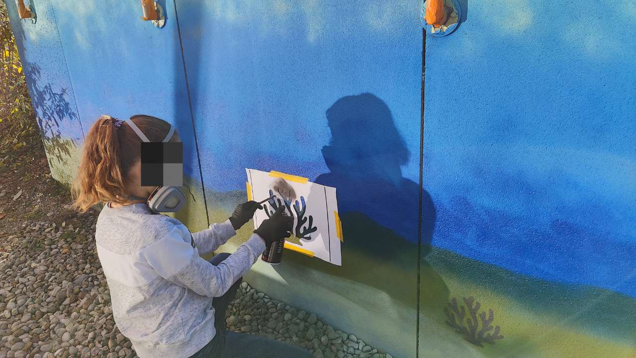 Kunstprojekt offene Jugendarbeit in Pöcking am Starnberger See. Thema des Streetart-Projektes "Unterwasserwelt" auf einer Betonmauer am Schwimmbad von Pöcking. Ein Mädchen sprüht die Schablone einer Koralle an die Wand.